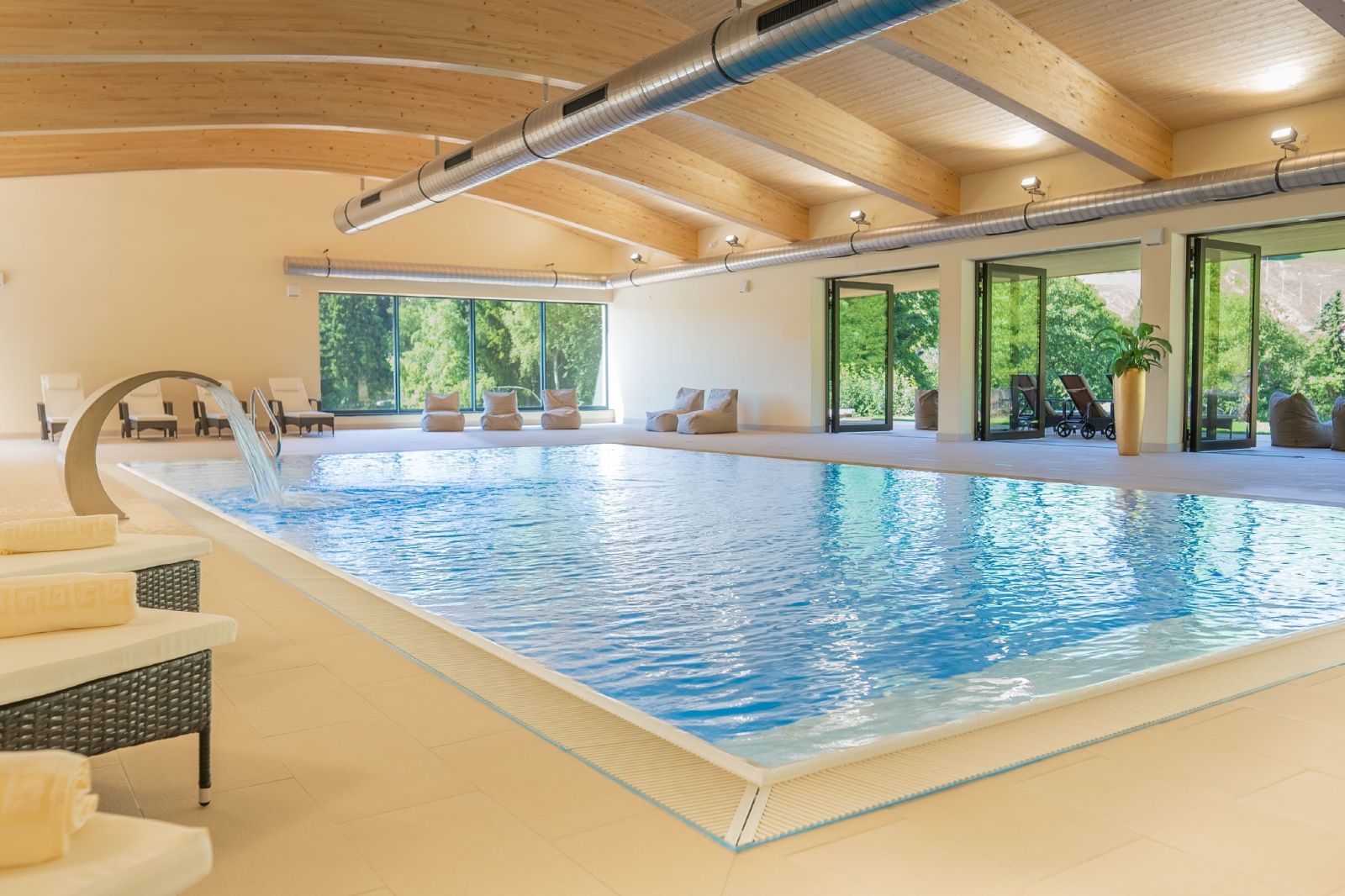 Swimming pool in a bright room with wooden ceiling and loungers